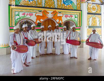 Des moines hindous (bhaktis) debout avec des tambours et des cymbales devant un mur et une porte sculptés de façon très élaborée. Majuli Island, Assam, Inde. Banque D'Images