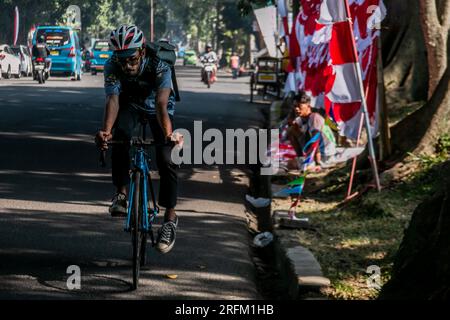 Bogor, Indonésie - 01 août 2023 : des cyclistes passent devant des commerçants avec des drapeaux rouges et blancs à Bogor, Java Ouest. Banque D'Images