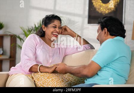 Couple indien détendu d'âge moyen parlant passer du temps en parlant les uns les autres sur le canapé à la maison - concept de communication, lien familial et Banque D'Images