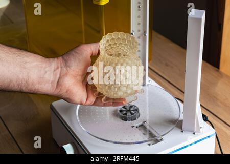 Homme tenant un objet en résine 3d avec à côté de lui une machine de cure Banque D'Images