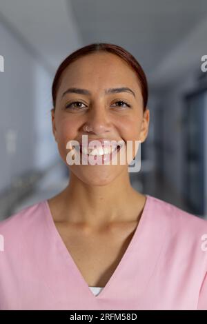 Portrait d'une femme biraciale heureuse médecin portant des gommages dans le couloir à l'hôpital Banque D'Images