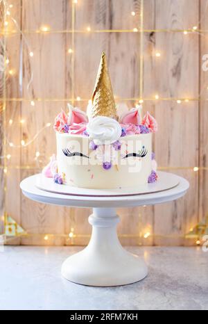 Magnifique gâteau licorne avec corne de gaufre dorée, cils et glaçage au fromage à la crème sur fond festif Banque D'Images