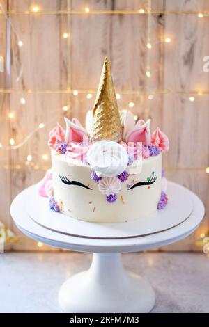 Magnifique gâteau licorne avec corne de gaufre dorée, cils et glaçage au fromage à la crème sur fond festif Banque D'Images