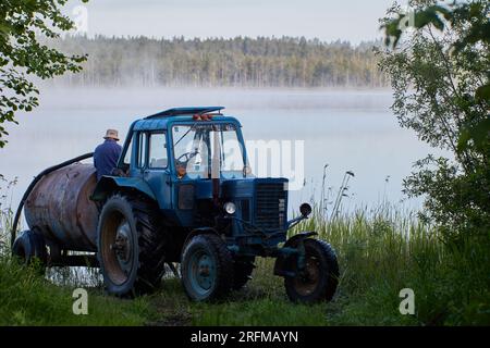 Ravitaillement du réservoir du tracteur avec de l'eau du lac forestier tôt le matin avec du brouillard. Banque D'Images
