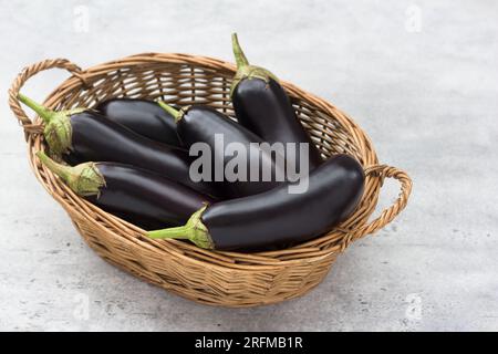 Panier en osier avec aubergines mûres et herbes sur fond gris texturé Banque D'Images