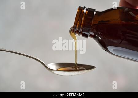 Verser le sirop à base de plantes d'une bouteille en verre sur une cuillère en métal, gros plan Banque D'Images