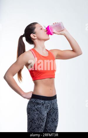 Au gymnase, une femme s'hydrate, son bras musclé exposé, soulignant l'importance de boire de l'eau pour atteindre la forme physique Banque D'Images