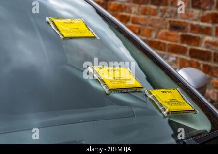 Billets de stationnement multiples ou avis de frais de pénalité sur le pare-brise d'une voiture garée dans la rue Banque D'Images