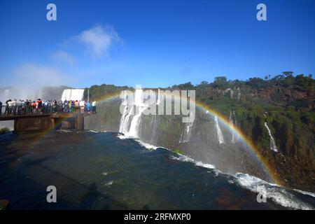 Touristes aux chutes d'Iguazu, l'une des grandes merveilles naturelles du monde, à la frontière du Brésil et de l'Argentine. Arc-en-ciel au premier plan Banque D'Images