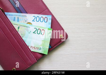 Billets de roubles russes dans un portefeuille en cuir. Portefeuille rouge Fucsia, sac à main. Fond en bois. Billets de banque. Argent en espèces. Fan de billets. FROTTER Banque D'Images