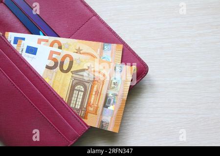 Cinquante billets d'euros dans un portefeuille en cuir. Portefeuille rouge Fucsia, sac à main. Fond en bois. Billets de banque. Argent en espèces Banque D'Images