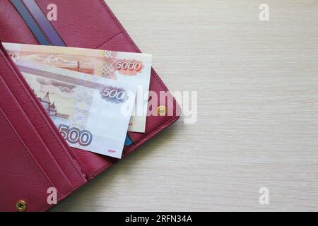 Billets de roubles russes dans un portefeuille en cuir. Portefeuille rouge Fucsia, sac à main. Fond en bois. Billets de banque Banque D'Images