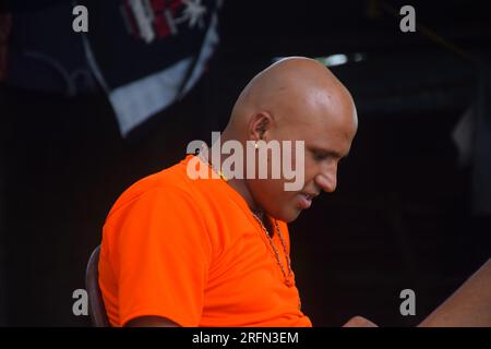 mignon modèle chauve portant un t-shirt orange, souriant regardant la caméra, avec fond noir Banque D'Images