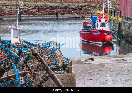 Dunbar Harbour sur la côte est de l'Écosse avec un bateau de pêche rouge amarré à un mur du port avec un autre bateau de pêche caché par des pots de homard. Banque D'Images