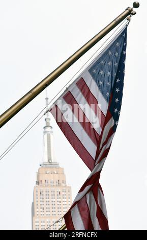Un drapeau américain tordu à rayures et étoiles est accroché devant l'Empire State Building à New York. Banque D'Images