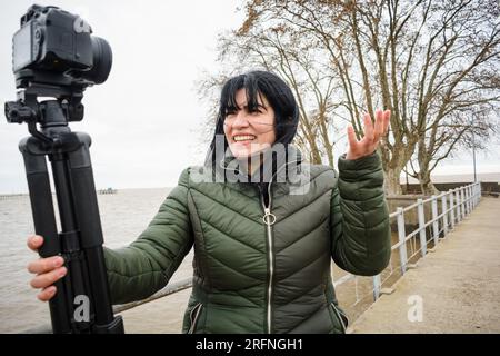 jeune vlogger vlogger vénézuélienne, souriant tenant sa caméra faisant une vidéo expliquant et parlant, debout sur une jetée du port d'olivos en bu Banque D'Images