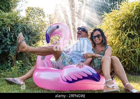 beau couple souriant d'âge moyen s'amusant assis sur le jouet gonflable rose flamant Banque D'Images