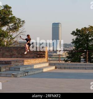 Une femme prend un selfie assis sur un mur dans le parc Kalemegdan / forteresse de Belgrade au-dessus de la rivière Sava à Belgrade, capitale de la Serbie. Le 4 août 2023, Banque D'Images
