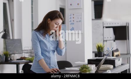 Jeune employé aux prises avec des maux de tête et travaillant sur ordinateur, frottant les tempes et se sentant inquiet de la douleur. Femme entrepreneure ayant une migraine douloureuse au bureau, travailler sous pression. Banque D'Images