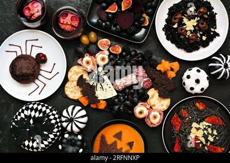 Scène de table de fête de dîner d'Halloween sur un fond noir. Vue de dessus. Planche de charcuterie effrayante, risotto noir et pâtes, gâteaux d'araignée, jack o lanterne Banque D'Images