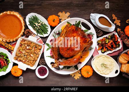 Dîner traditionnel à la dinde de Thanksgiving. Scène de table vue aérienne sur un fond de bois sombre. Dinde, purée de pommes de terre, farce, tarte à la citrouille et accompagnements. Banque D'Images