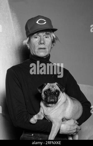 Andy Warhol pose en portant une casquette de baseball Cincinnati Reds tout en tenant un chien de race chiot en 1982. Warhol était un artiste visuel américain, réalisateur, producteur et figure de proue du mouvement pop art. Ses œuvres explorent la relation entre l'expression artistique, la publicité et la culture des célébrités qui a prospéré dans les années 1960, et couvrent une variété de médias, y compris la peinture, la sérigraphie, la photographie, le cinéma, et sculpture. Parmi ses œuvres les plus connues figurent les peintures sérigraphiées Campbell's Soup Cans et Marilyn diptyque. Photo de Bernard Gotfryd Banque D'Images