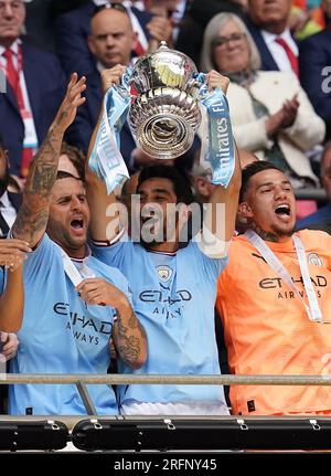 Le capitaine de Manchester City Ilkay Gundogan lève le trophée de la FA Cup avec Kyle Walker (à gauche) et le gardien de but Ederson (à droite) alors qu'ils célèbrent la victoire de la finale de la FA Cup des Emirates au stade de Wembley, à Londres. Date de la photo : Samedi 3 juin 2023. Voir PA Story FOOTBALL final. Le crédit photo devrait se lire : Nick Potts/PA Wire. RESTRICTIONS : USAGE ÉDITORIAL UNIQUEMENT pas d'utilisation avec des fichiers audio, vidéo, données, listes de rencontres, logos de club/ligue ou services « live » non autorisés. Utilisation en ligne limitée à 120 images, pas d'émulation vidéo. Aucune utilisation dans les Paris, les jeux ou les publications individuelles de club/ligue/joueur. Banque D'Images