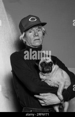 Andy Warhol pose en portant une casquette de baseball Cincinnati Reds tout en tenant un chien de race chiot en 1982. Warhol était un artiste visuel américain, réalisateur, producteur et figure de proue du mouvement pop art. Ses œuvres explorent la relation entre l'expression artistique, la publicité et la culture des célébrités qui a prospéré dans les années 1960, et couvrent une variété de médias, y compris la peinture, la sérigraphie, la photographie, le cinéma, et sculpture. Parmi ses œuvres les plus connues figurent les peintures sérigraphiées Campbell's Soup Cans et Marilyn diptyque. Photo de Bernard Gotfryd Banque D'Images