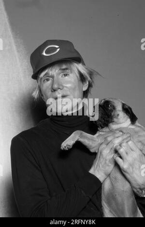 Andy Warhol pose en portant une casquette de baseball Cincinnati Reds tout en tenant un chien de race chiot en 1982. Warhol était un artiste visuel américain, réalisateur, producteur et figure de proue du mouvement pop art. Ses œuvres explorent la relation entre l'expression artistique, la publicité et la culture des célébrités qui a prospéré dans les années 1960, et couvrent une variété de médias, y compris la peinture, la sérigraphie, la photographie, le cinéma, et sculpture. Parmi ses œuvres les plus connues figurent les peintures sérigraphiées Campbell's Soup Cans et Marilyn diptyque. Photo de Bernard Gotfryd Banque D'Images