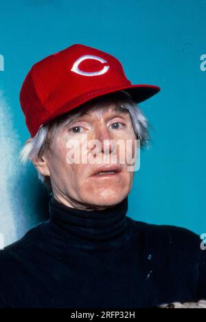 Andy Warhol pose en portant une casquette de baseball Cincinnati Reds tout en tenant un chien de race chiot en 1982. Warhol était un artiste visuel américain, réalisateur, producteur et figure de proue du mouvement pop art. Ses œuvres explorent la relation entre l'expression artistique, la publicité et la culture des célébrités qui a prospéré dans les années 1960, et couvrent une variété de médias, y compris la peinture, la sérigraphie, la photographie, le cinéma, et sculpture. Parmi ses œuvres les plus connues figurent les peintures sérigraphiées Campbell's Soup Cans et Marilyn diptyque. Photo de Bernard Gotfryd Banque D'Images