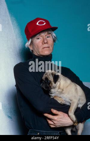 Andy Warhol pose en portant une casquette de baseball Cincinnati Reds tout en tenant un chien de race chiot en 1982. Warhol était un artiste visuel américain, réalisateur, producteur et figure de proue du mouvement pop art. Ses œuvres explorent la relation entre l'expression artistique, la publicité et la culture des célébrités qui a prospéré dans les années 1960, et couvrent une variété de médias, y compris la peinture, la sérigraphie, la photographie, le cinéma, et sculpture. Parmi ses œuvres les plus connues figurent les peintures sérigraphiées Campbell's Soup Cans et Marilyn diptyque. Photo de Bernard Gotfryd Banque D'Images