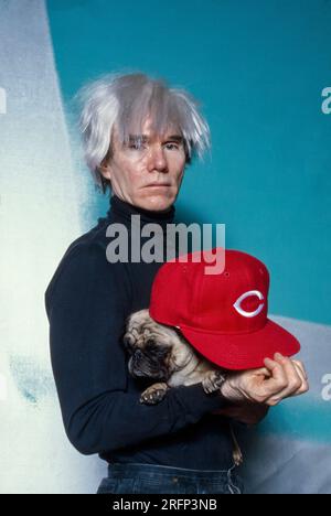 Andy Warhol pose en portant une casquette de baseball Cincinnati Reds tout en tenant un chien de race chiot en 1982. Warhol était un artiste visuel américain, réalisateur, producteur et figure de proue du mouvement pop art. Ses œuvres explorent la relation entre l'expression artistique, la publicité et la culture des célébrités qui a prospéré dans les années 1960, et couvrent une variété de médias, y compris la peinture, la sérigraphie, la photographie, le cinéma, et sculpture. Parmi ses œuvres les plus connues figurent les peintures sérigraphiées Campbell's Soup Cans et Marilyn diptyque. Photo de Bernard Gotfryd Banque D'Images