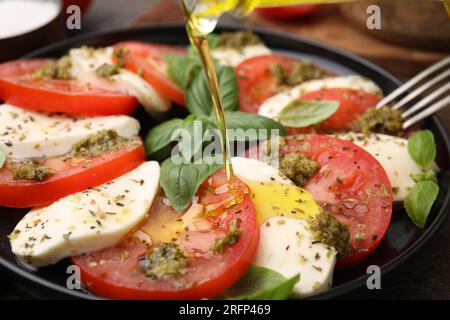 Verser l'huile d'olive sur la délicieuse salade Caprese avec sauce pesto sur la table, gros plan Banque D'Images