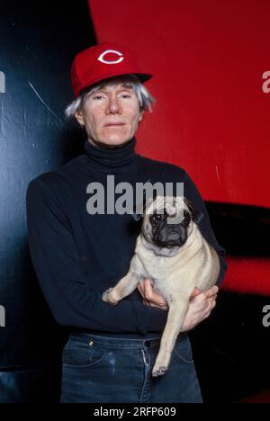 Andy Warhol pose en portant une casquette de baseball Cincinnati Reds tout en tenant un chien de race chiot en 1982. Warhol était un artiste visuel américain, réalisateur, producteur et figure de proue du mouvement pop art. Ses œuvres explorent la relation entre l'expression artistique, la publicité et la culture des célébrités qui a prospéré dans les années 1960, et couvrent une variété de médias, y compris la peinture, la sérigraphie, la photographie, le cinéma, et sculpture. Parmi ses œuvres les plus connues figurent les peintures sérigraphiées Campbell's Soup Cans et Marilyn diptyque. Photo de Bernard Gotfryd Banque D'Images