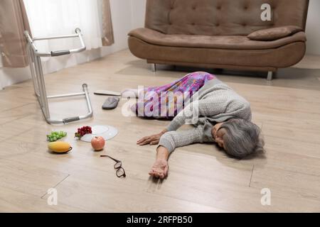 La femme âgée tombe à cause de l'hypertension dans le salon. Banque D'Images