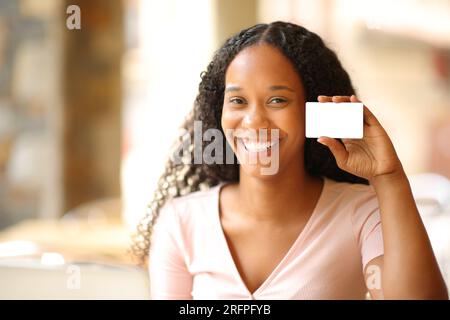 Femme noire heureuse montrant carte de crédit vierge dans une terrasse de bar Banque D'Images