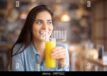 Femme heureuse buvant du jus d'orange regarde loin dans un intérieur de bar Banque D'Images