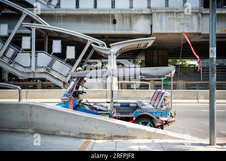 Un tuk tuk thaï classique attend devant la station aérienne de Chong Nonsi BTS dans le quartier de Chong Nonsi à Bangkok, en Thaïlande. Banque D'Images