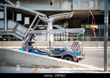 Un tuk tuk thaï classique attend devant la station aérienne de Chong Nonsi BTS dans le quartier de Chong Nonsi à Bangkok, en Thaïlande. Banque D'Images