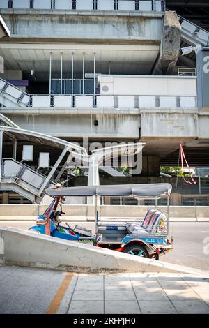 Un tuk tuk thaï classique attend devant la station aérienne de Chong Nonsi BTS dans le quartier de Chong Nonsi à Bangkok, en Thaïlande. Banque D'Images