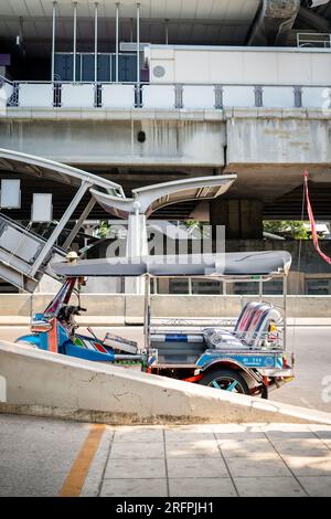 Un tuk tuk thaï classique attend devant la station aérienne de Chong Nonsi BTS dans le quartier de Chong Nonsi à Bangkok, en Thaïlande. Banque D'Images