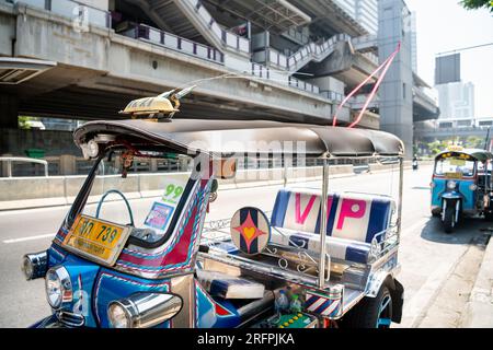 Un tuk tuk thaï classique attend devant la station aérienne de Chong Nonsi BTS dans le quartier de Chong Nonsi à Bangkok, en Thaïlande. Banque D'Images