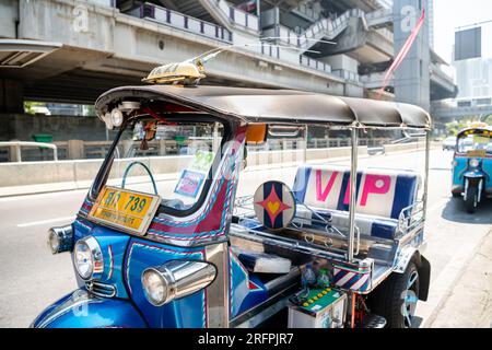 Un tuk tuk thaï classique attend devant la station aérienne de Chong Nonsi BTS dans le quartier de Chong Nonsi à Bangkok, en Thaïlande. Banque D'Images