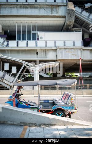 Un tuk tuk thaï classique attend devant la station aérienne de Chong Nonsi BTS dans le quartier de Chong Nonsi à Bangkok, en Thaïlande. Banque D'Images