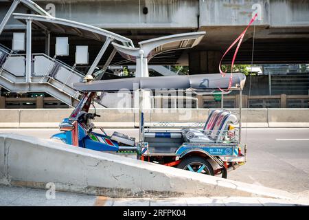 Un tuk tuk thaï classique attend devant la station aérienne de Chong Nonsi BTS dans le quartier de Chong Nonsi à Bangkok, en Thaïlande. Banque D'Images