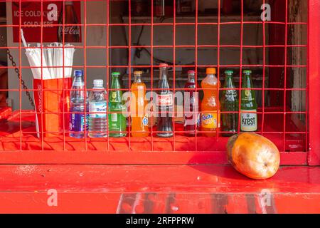 Alignement de bouteilles offrant diverses boissons derrière la clôture d'un magasin rouge fermé. Jinja, Ouganda. Banque D'Images