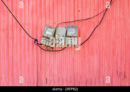 Compteurs électriques accrochés négligemment sur un mur de tôle rose. Jinja, Ouganda. Banque D'Images