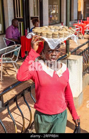 Jeune fille portant un plateau de cupcakes sur sa tête. Jinja, Ouganda. Banque D'Images