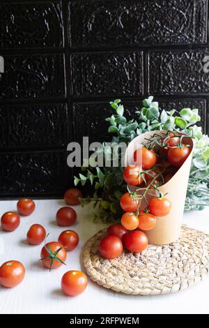 Vue de face d'un emballage en carton contenant des tomates cerises. Concept zéro plastique. Fond noir et table blanche. Banque D'Images