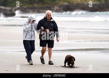 Promeneurs de chiens sur la plage de Carne en Cornouailles, comme un avertissement de danger pour la vie a été émis alors que la tempête Antoni frappe certaines parties du Royaume-Uni, apportant de fortes pluies et des vents forts. Date de la photo : Samedi 5 août 2023. Banque D'Images